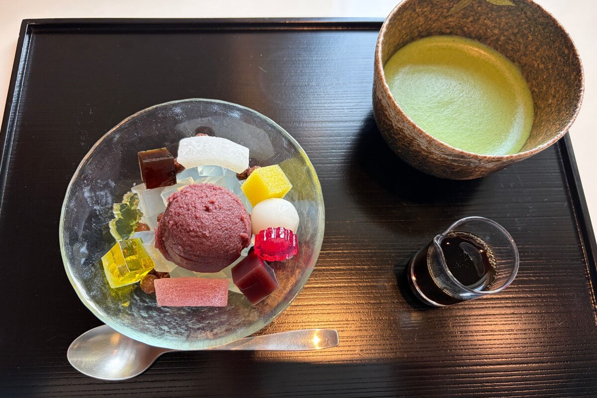 とらやのあんみつと抹茶。ガラスの器にあんこと白玉、色とりどりの寒天。横に黒蜜の小瓶が黒い盆にのっている